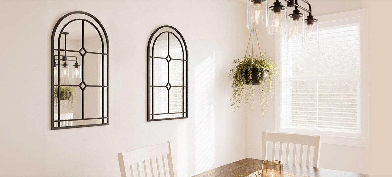 Two black arched Saliwa mirrors hung in a sunlit white-walled dining room.