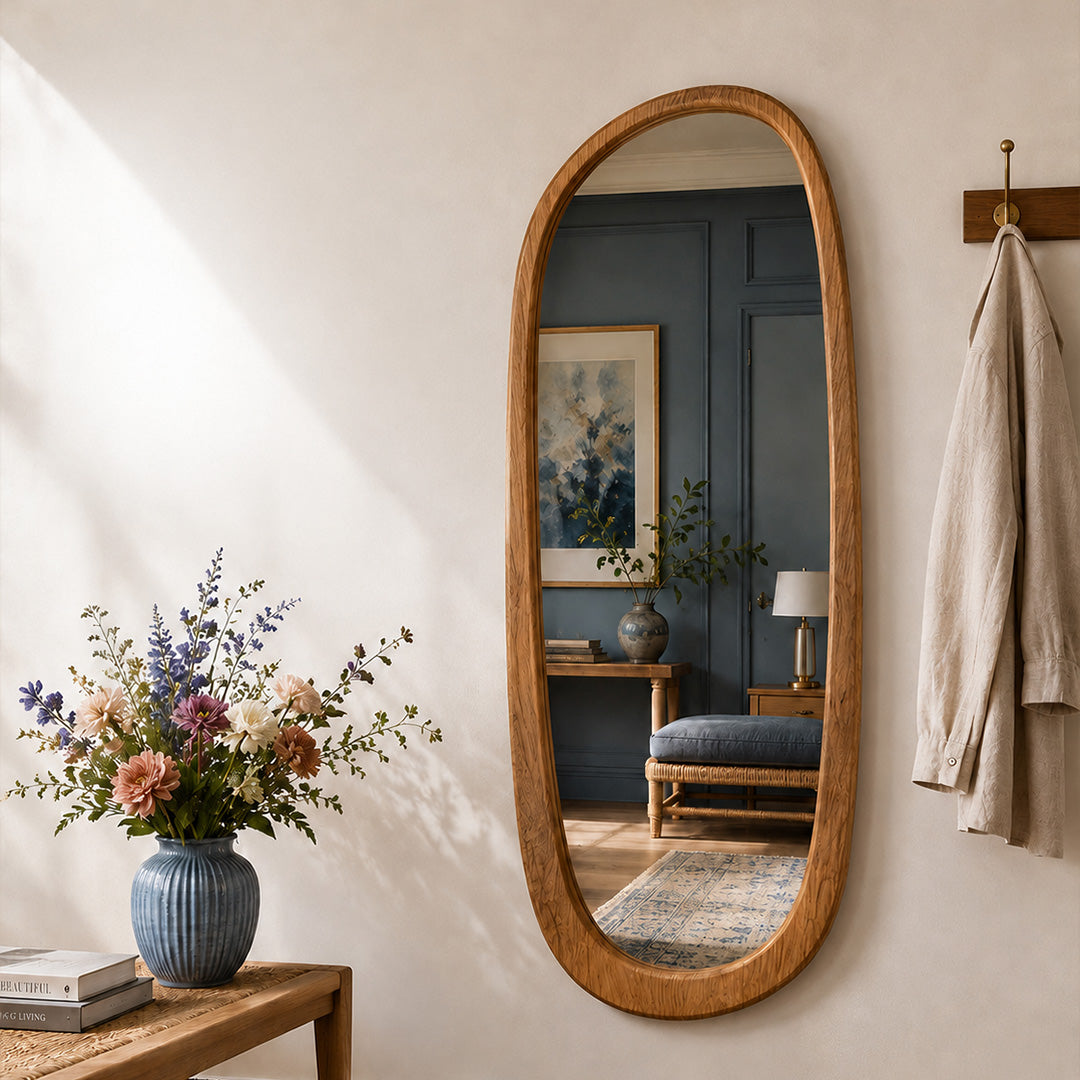 A honey-wood oval Saliwa mirror in a cream entryway, reflecting a blue-paneled room and framed artwork.